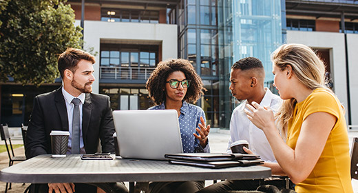 Coworkers sitting outside at a table and discussing a work project