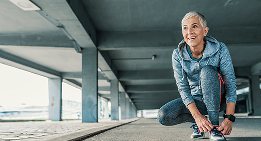Older woman in running attire stopping to kneel down and tie her shoes
