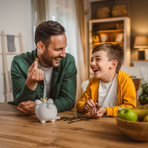 father and son saving change in a piggy bank_480x480