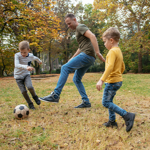 father and his two sons play soccer in the yard_480x480